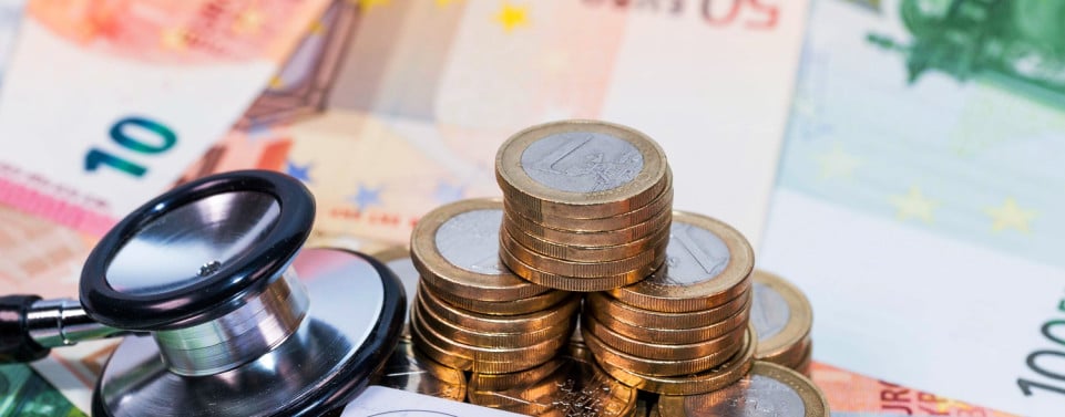 Krankenkassenkarte, Stethoskop und ein mehrere Münzen liegen auf Eurogeldscheinen.